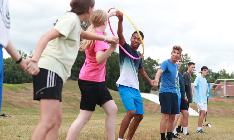 Students hand in hand in a long row try to pass a hula hoop along without breaking the chain