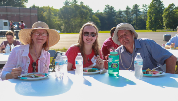 A student with her parents at the outdoor picnic dinner table 