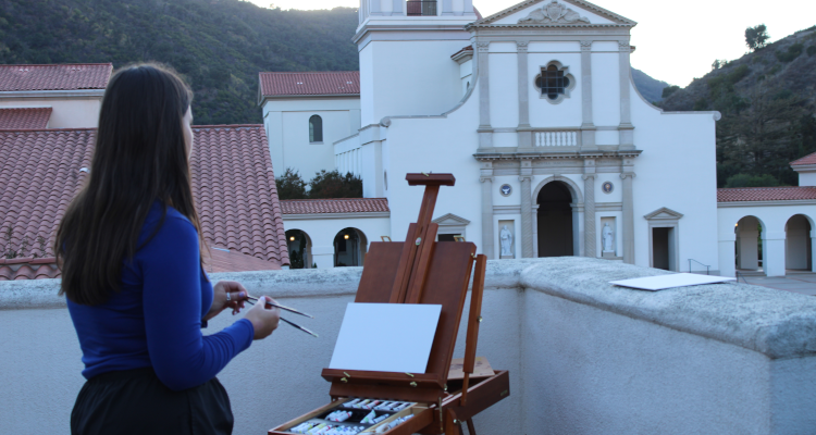 A student paints the Chapel on an easel as the sun sets