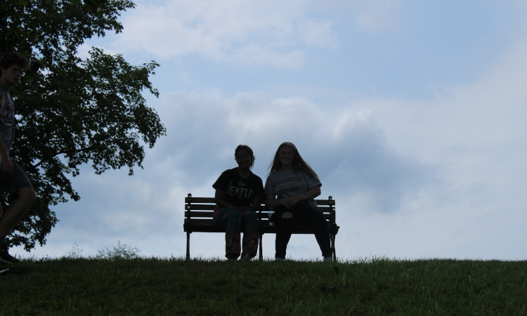 Silhouette: two students on a bench against the sky