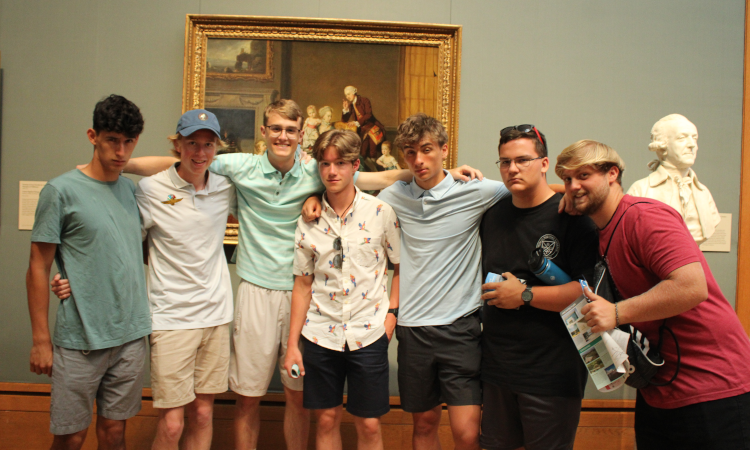 Seven students pose in front of a painting