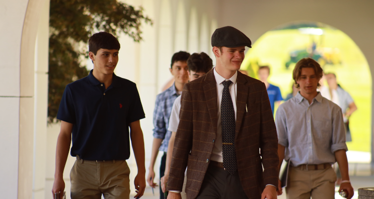 Several walk under the arcade, one in a flat cap and brown plaid