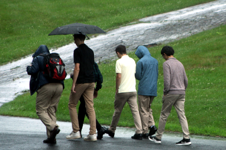 Students walk across campus in the rain, carrying umbrellas