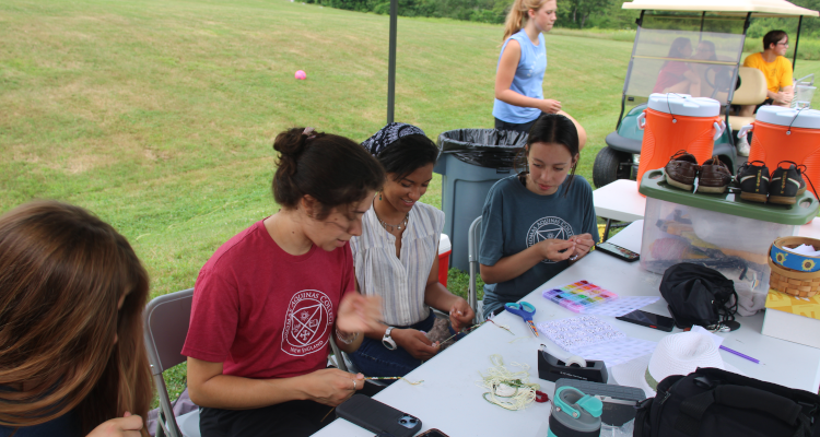 Students do arts and crafts at a shaded outdoor table