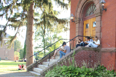 Students read on the staircase to a red-brick building