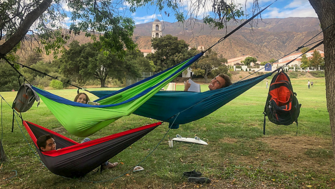 Three students rest in hammocks, with Our Lady of the Most Holy Trinity Chapel in the background