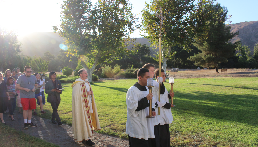 Fr. Paul leads a Nativity of Mary procession, behind cross and candles