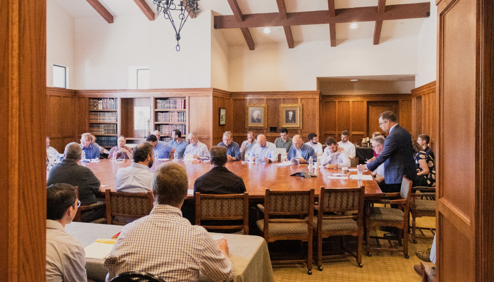 Long shot of the tutors around the table, with two at a smaller table off to one side