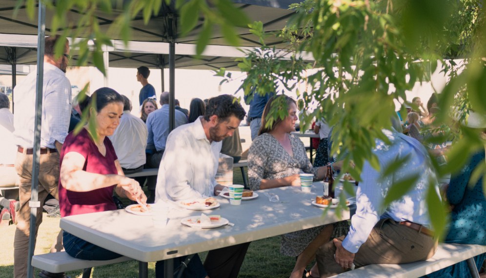 Tutors and families gather at benches under canopies for an outdoor lunch