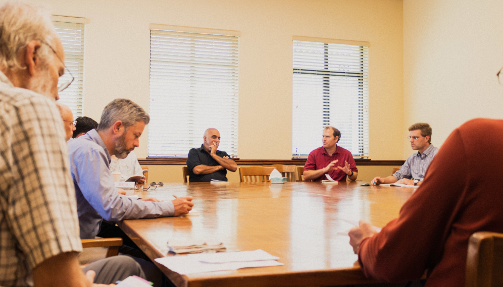 Around the table: a tutor takes notes in the foreground while others discuss