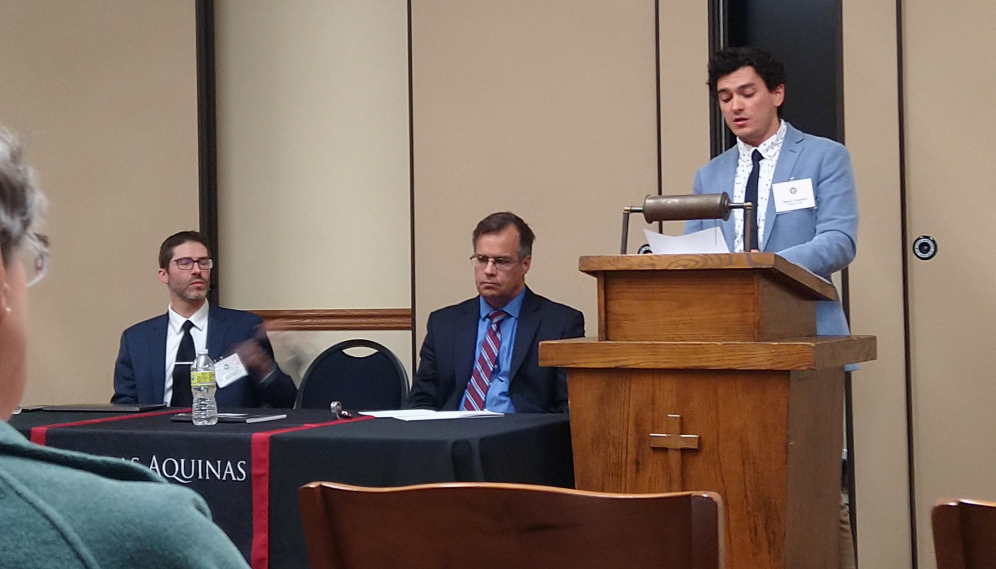 A speaker delivers their address, with a panel off to the left