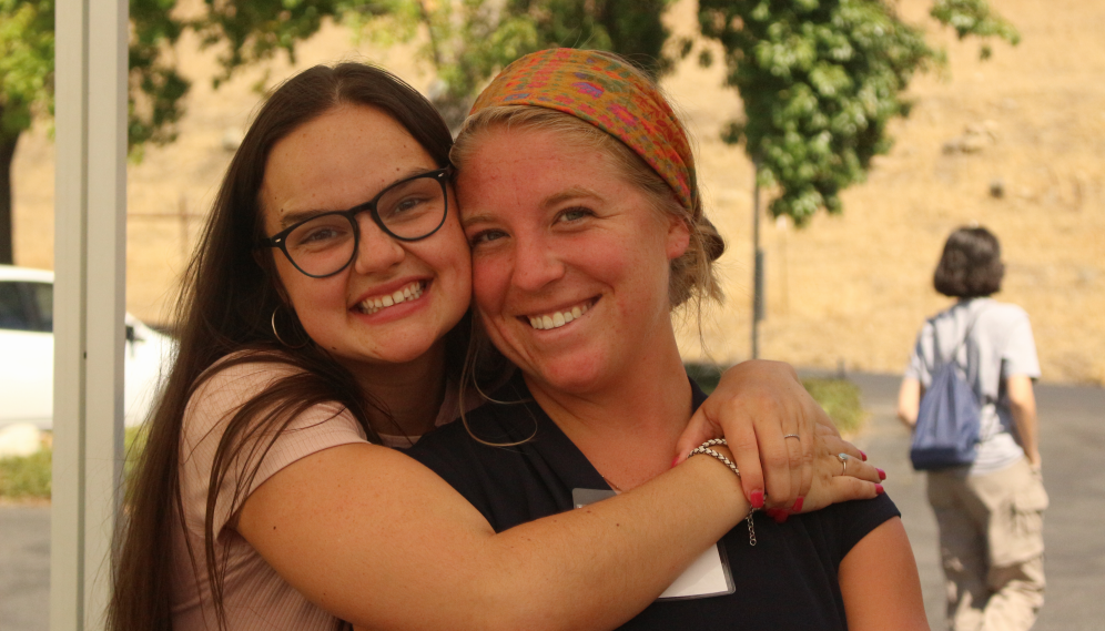 A freshman hugs her mother; both smile for the camera