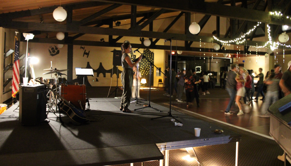 A girl sings at the mic while students dance in the background