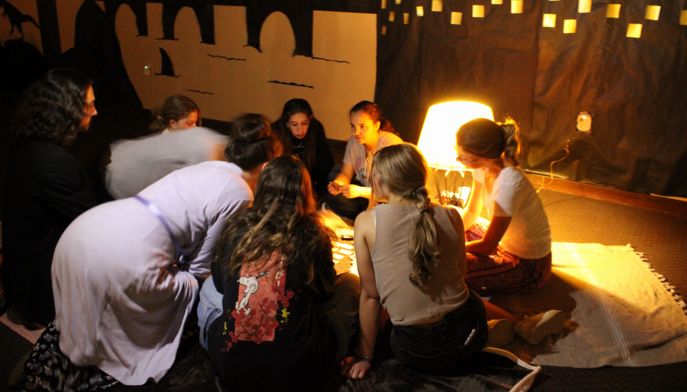 A circle of students seated on the floor, playing a card game