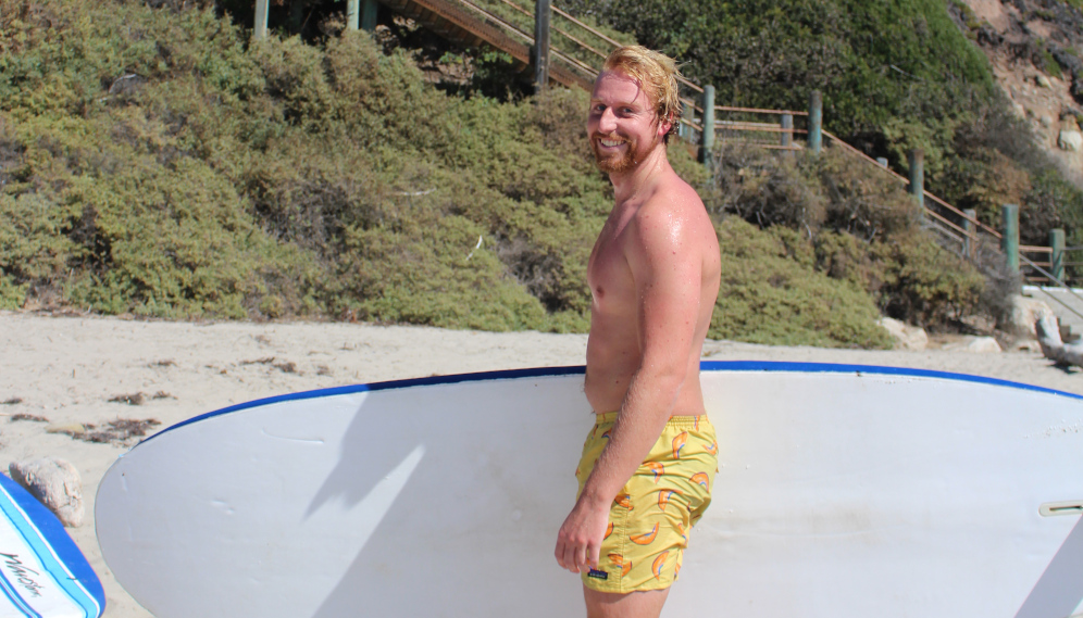 A student holding a surfboard smiles for the camera