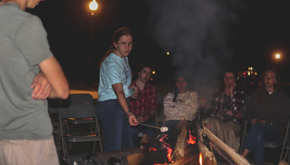 A student roasts a marshmallow over the campfire