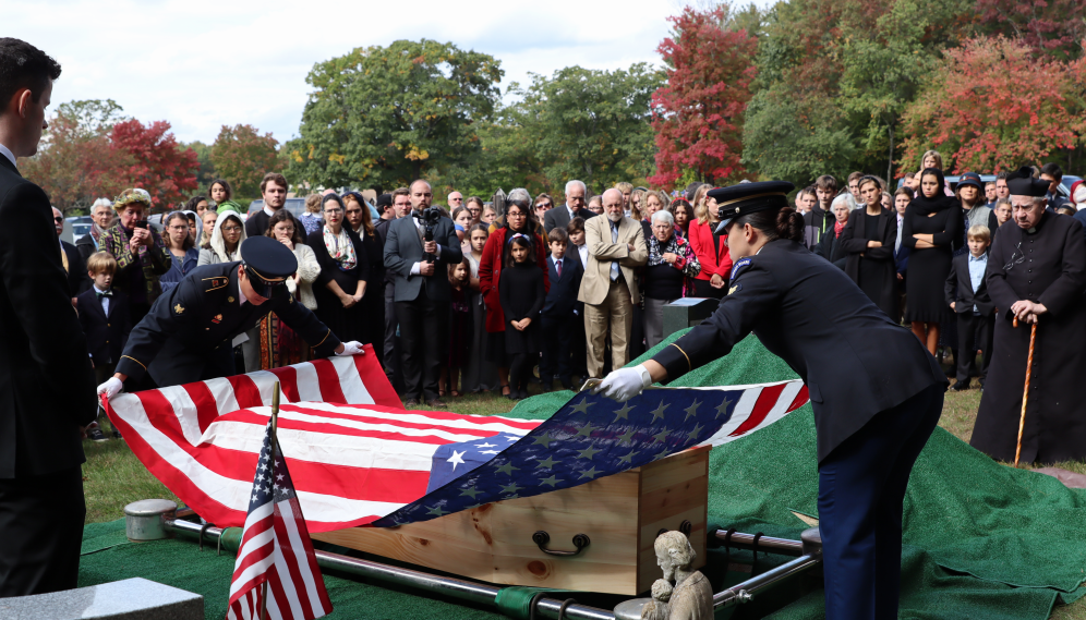 Two members of the military remove the flag from the casket...