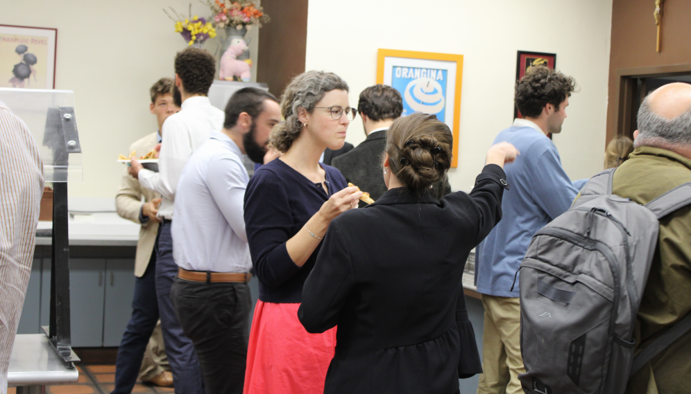 Students and tutors chat near the pizza serving line after the seminar