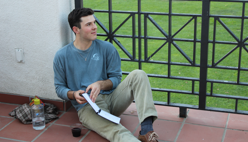 A student sits on the tiles with his notebook