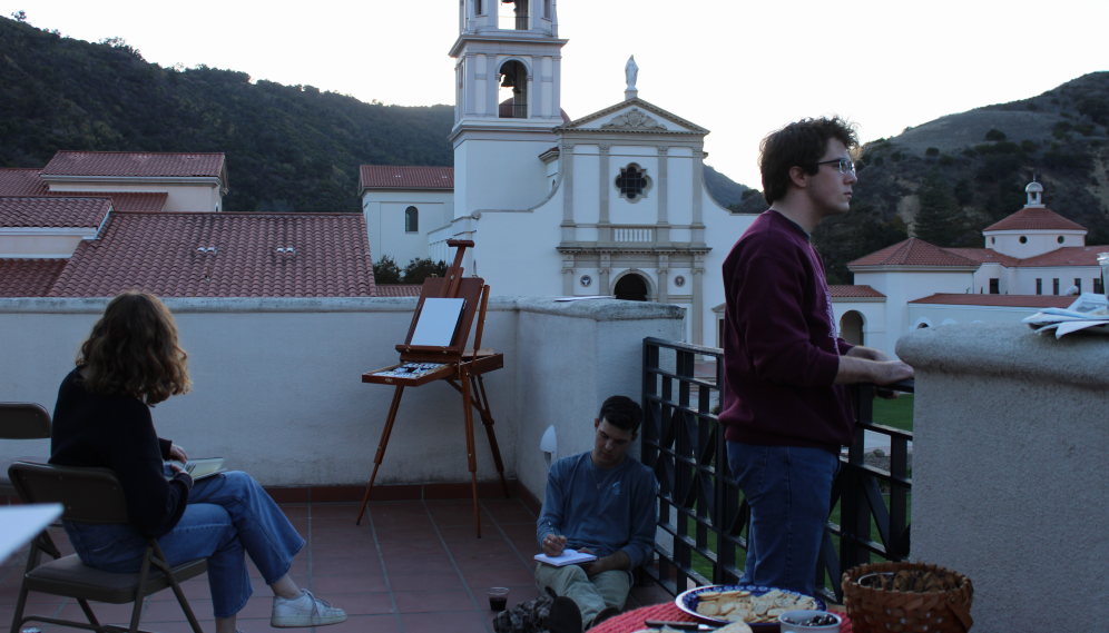 Students on the library balcony paint and watch the sunset