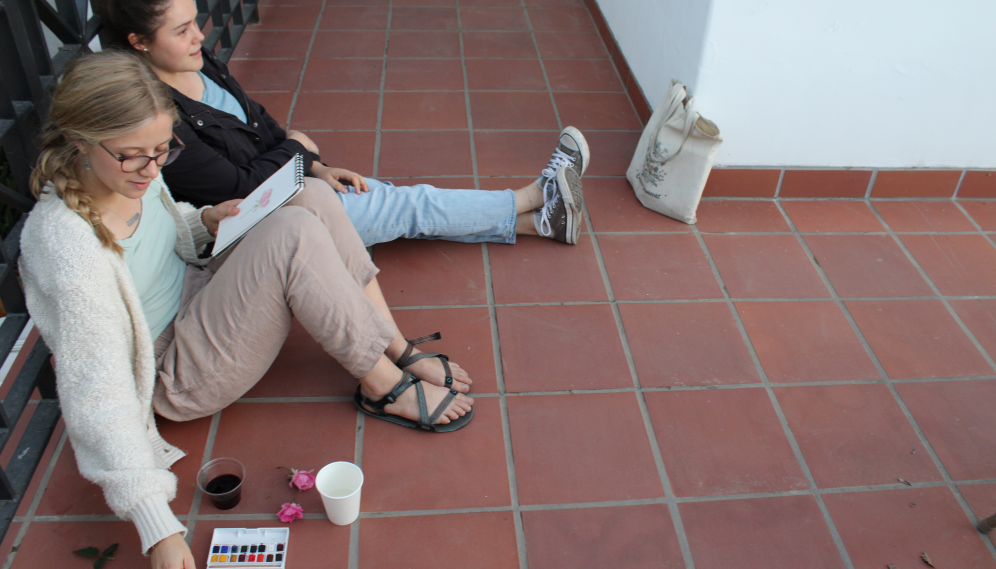 Seated on the floor, a student paints with her friend