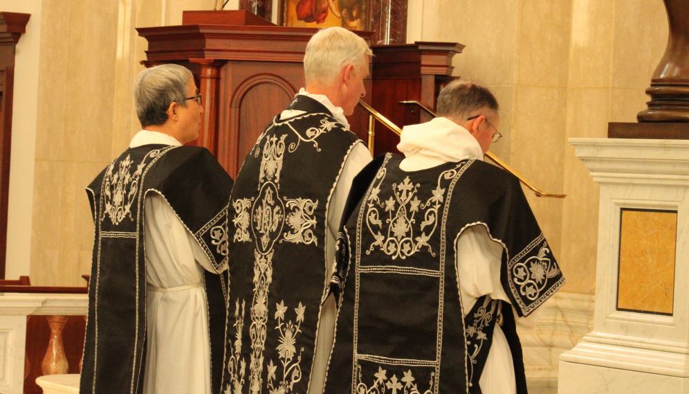Three priests kneel before the altar