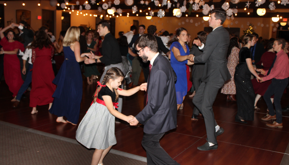 Student pairs dance in the background; in the foreground a student dances with a tutor kid