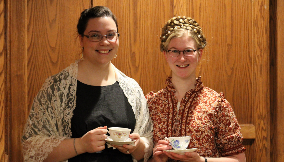 Two pose for a photo, teacups in hand