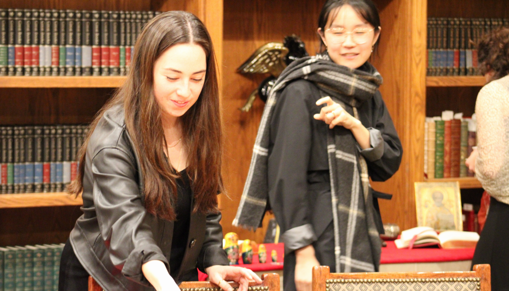 Two get tea at the table, with Matryoshka dolls visible in the background