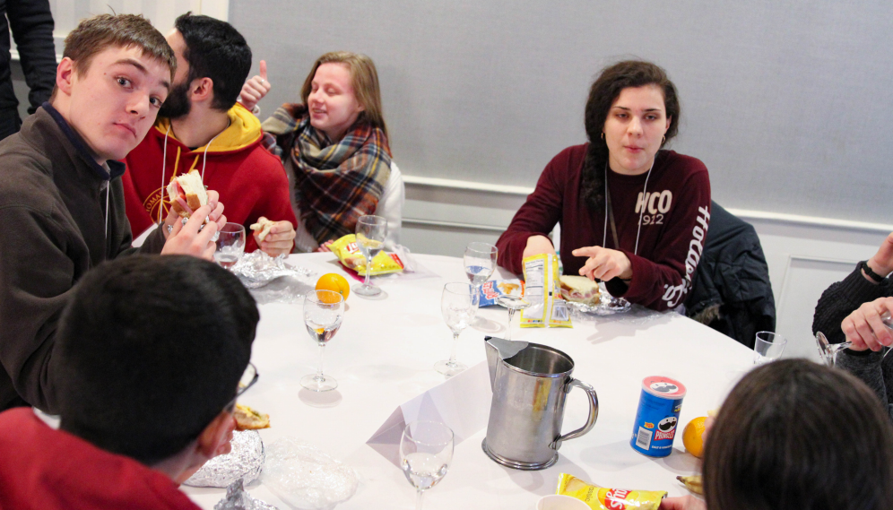 Students eat sandwiches and chips at a round table indoors
