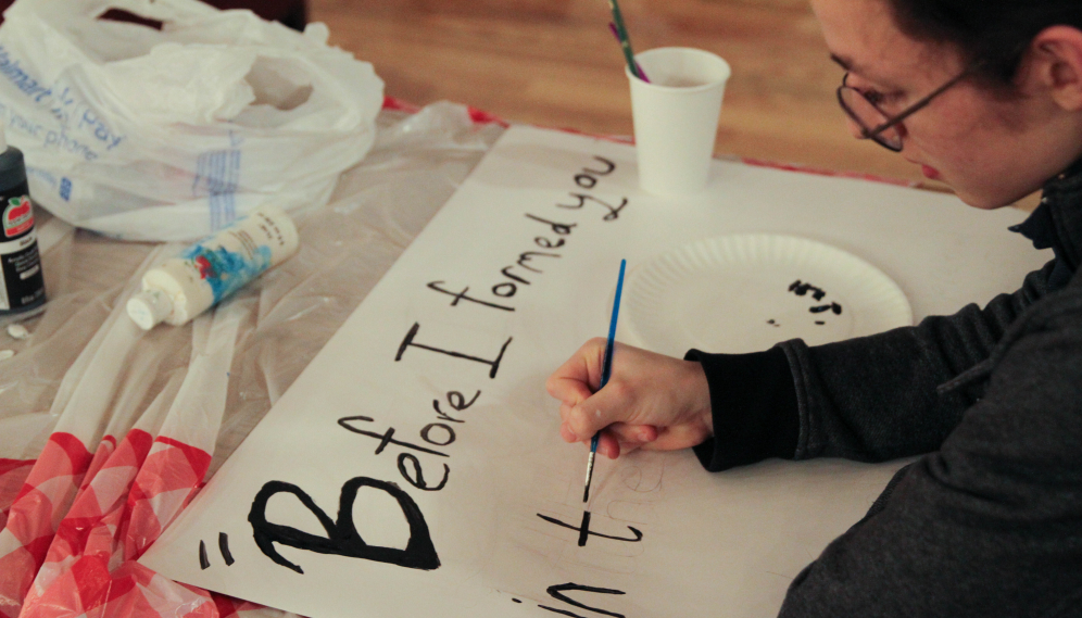 A student paints a pro-life sign with "Before I formed you in the womb..."