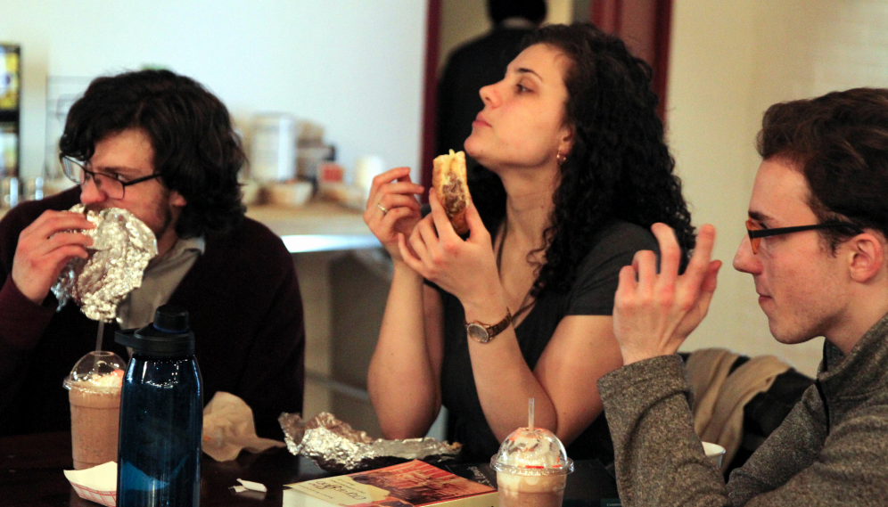 Three at a table, eating cheesesteaks