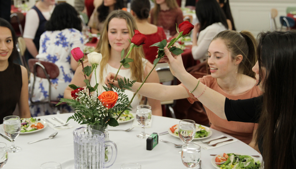 The girls admire the roses in the vase at the center of the table