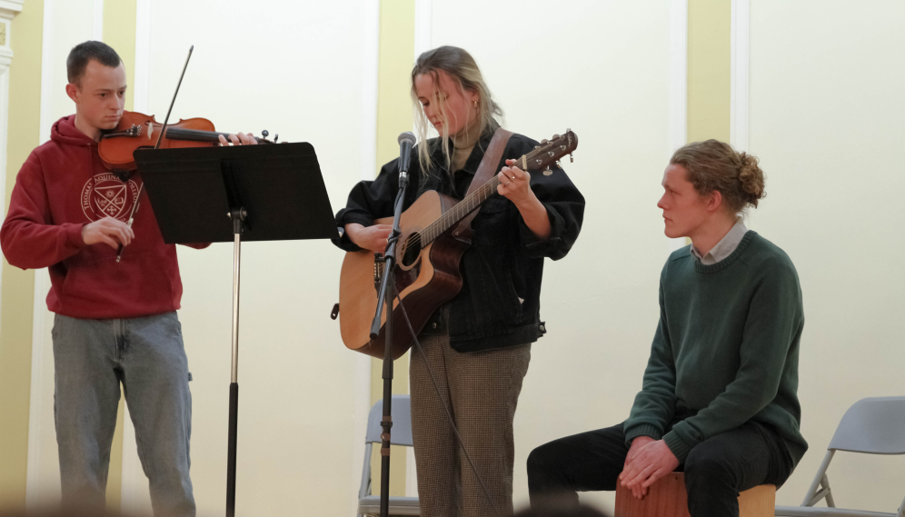 A violinist, guitarist, and drummer perform