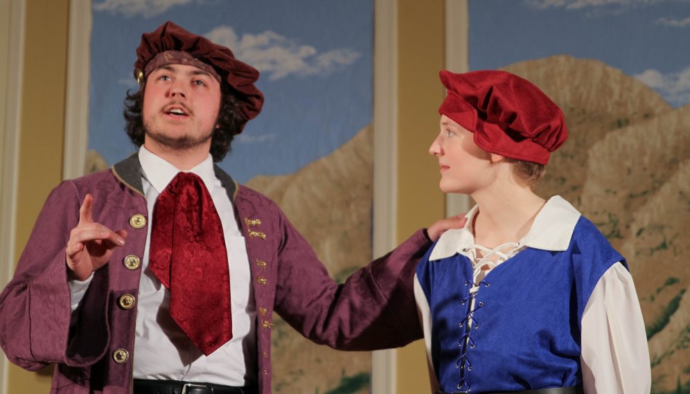 A lady in red, white, and blue talks with a man in a red cravat