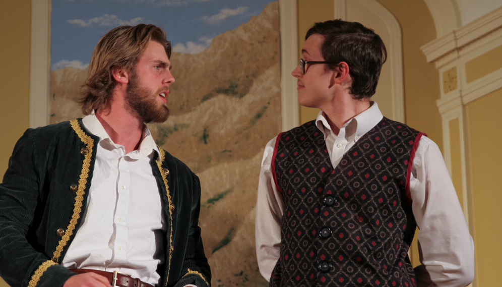 Malvolio (a tall thin man in a diamond-patterned vest) converses with the sailor-jacketed man