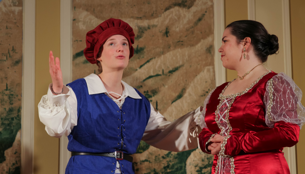 The Lady Olivia, now dressed in resplendent red satin, converses with the servant in the puffy red cap