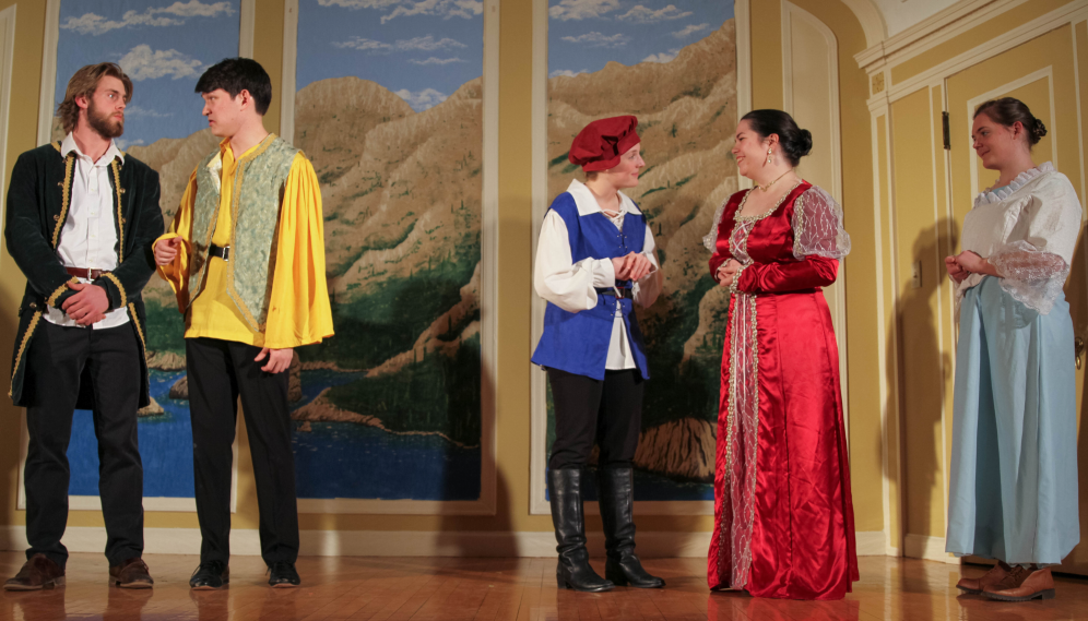 The sailor-jacketed man converses with the man in yellow, the Lady Olivia converses with the girl with the puffy cap, and the girl in lace looks on smiling