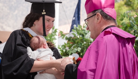 A married graduate, baby in hand, receives her diploma