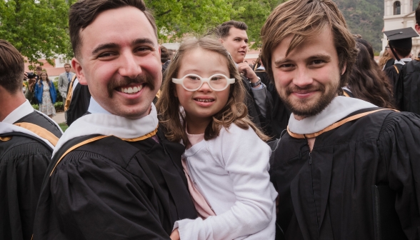 Two graduates, one holding a child, pose for a photo