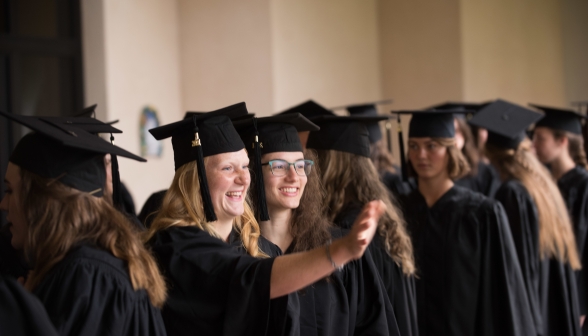 A graduate waves to someone out of frame