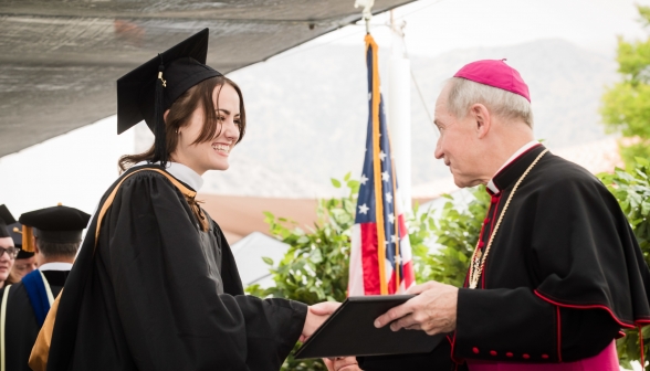 A graduate shakes hands with the Bishop as she receives her diploma