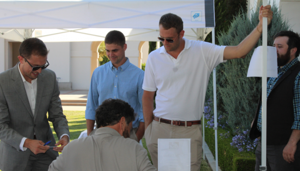 Three graduates look on while another applies a name tag to himself
