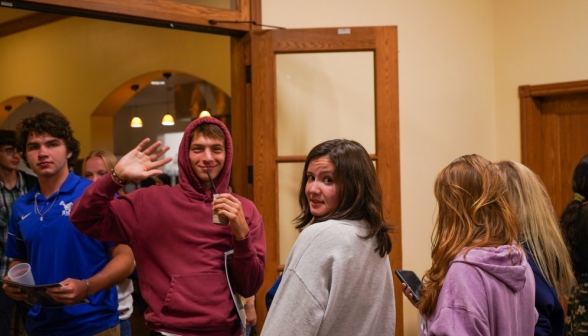 A student waves to the camera while sipping a drink