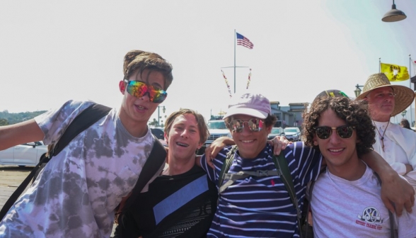 Four others pose for a photo, one cocking an eyebrow behind rainbow shades