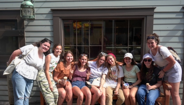 Nine girls seated afront the window of a clapboard building