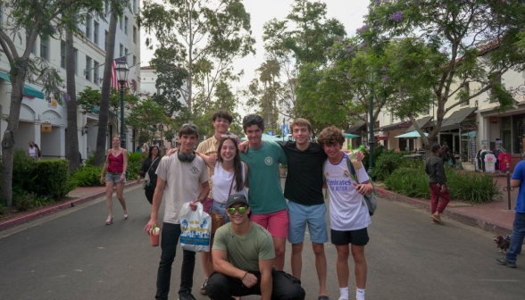 Seven students posing in center frame. We are looking straight down a shaded street with wide tiled sidewalks