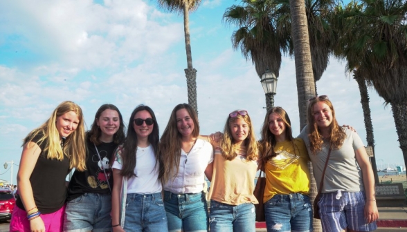Seven girls link arms against the backdrop of the California sky