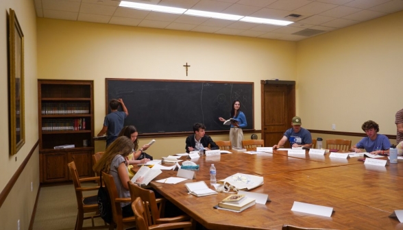 Pre-class, two students practice props at either end of the blackboard, while others study at the table