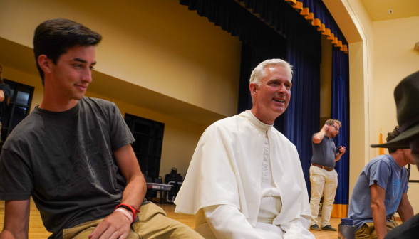 A student sitting with Fr. Walshe on the edge of the stage